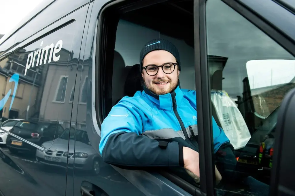 A Amazon employee sitting in the drivers seat of his Amazon delivery van.