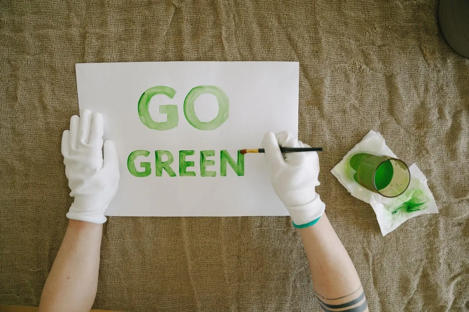 A person using a paint brush to paint the words "Go Green" in green paint on a piece of paper.