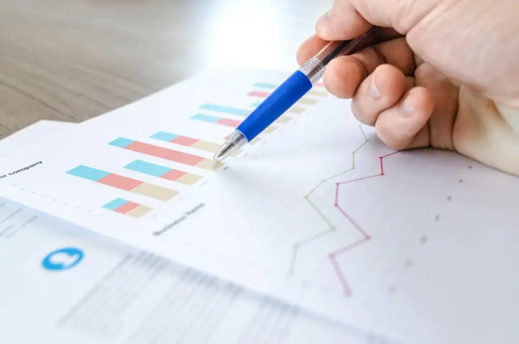 A persons hand using a pen to point at a piece of paper with a bar chart and line graph on it.