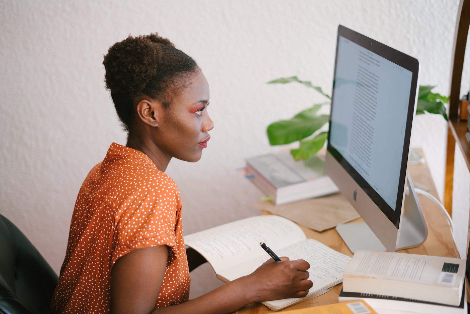 photo of woman looking on computer while taking notes in her notebook.