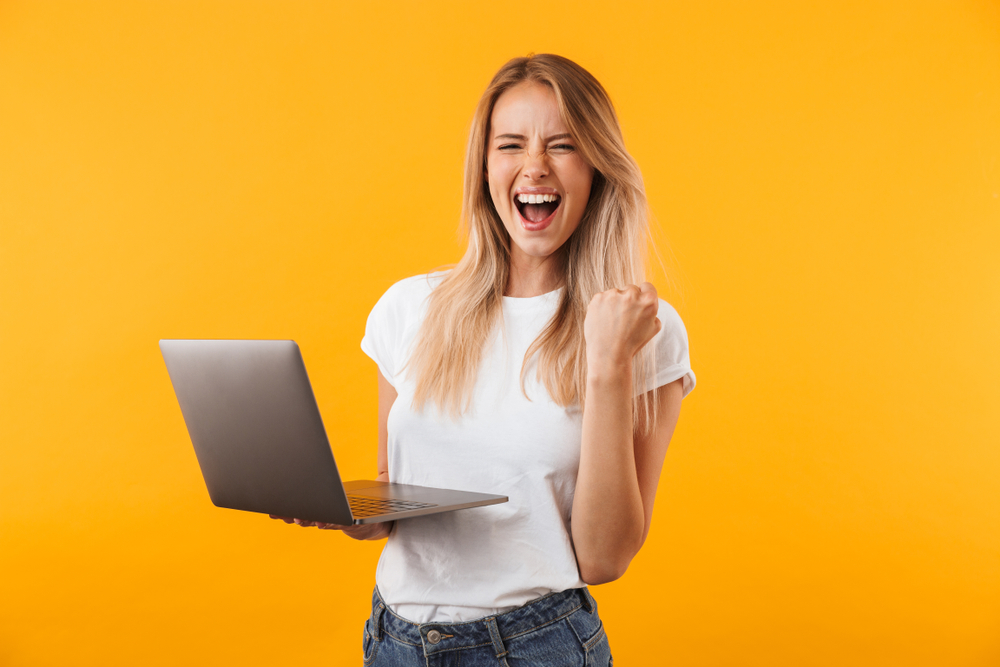Woman holding a laptop pumping her fist with joy.